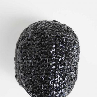 Black fencing mask with shiny black jewels adhered to the entire surface catching the light