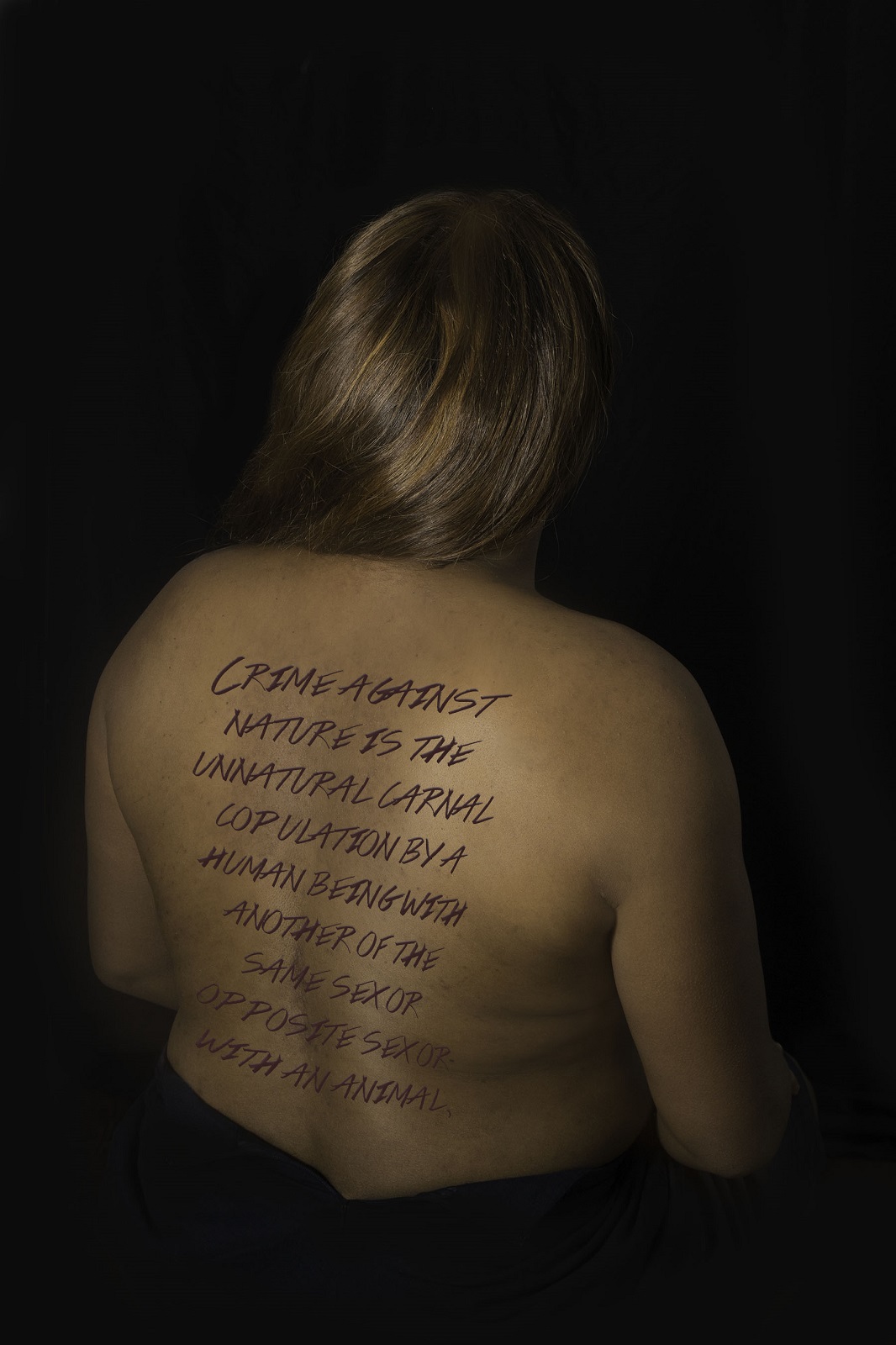 Photograph of a dark skinned woman wiht her back exposed, not wearing a shirt, with writing on her back