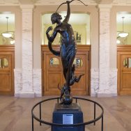 Bronze sulpture of a nude woman wiht her arm raised in the air with a archery bow, and a small dog at her feet