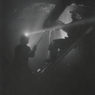 black and white photo of inside a mine, with two figures extracting ore, with headlamps on