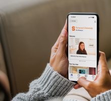 A woman on a couch holding her phone with the SU Art Museum digital guide from Bloomberg Connects open.