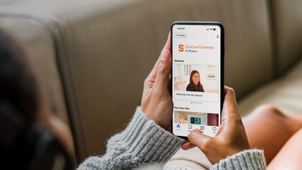 A woman on a couch holding her phone with the SU Art Museum digital guide from Bloomberg Connects open.