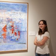 Charlotte Bingham stands by an abstract painting in a museum gallery.
