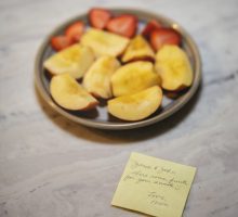 A photography of a plate of strawberries and peaches, sliced, and a sticky note.