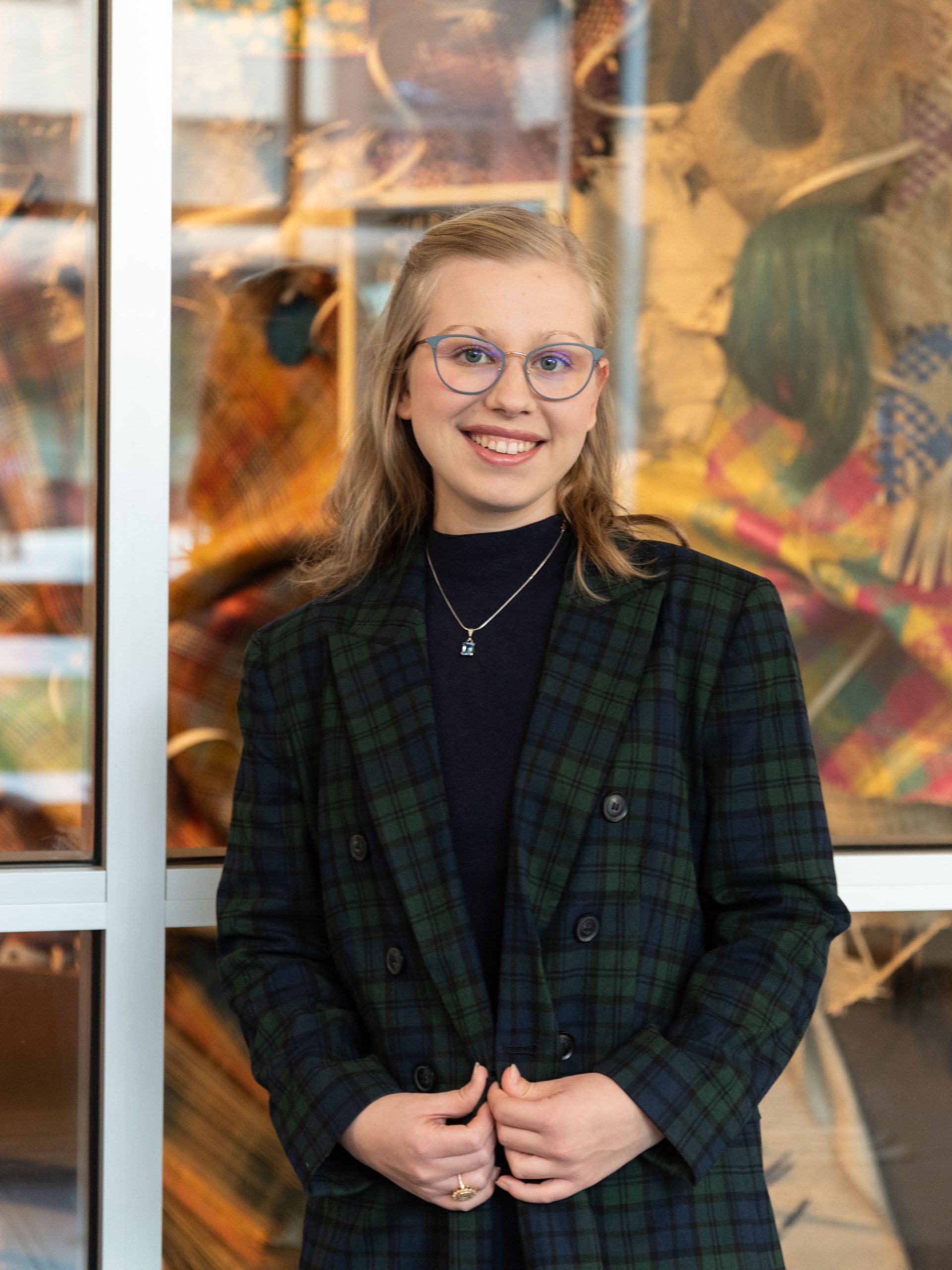 Portrait of graduate student with light hair wearing a dark, plaid suit.